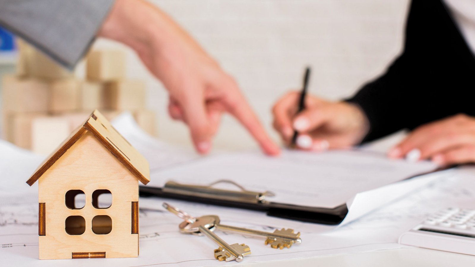 Close-up of a housing contract being signed next to homeownership symbols.